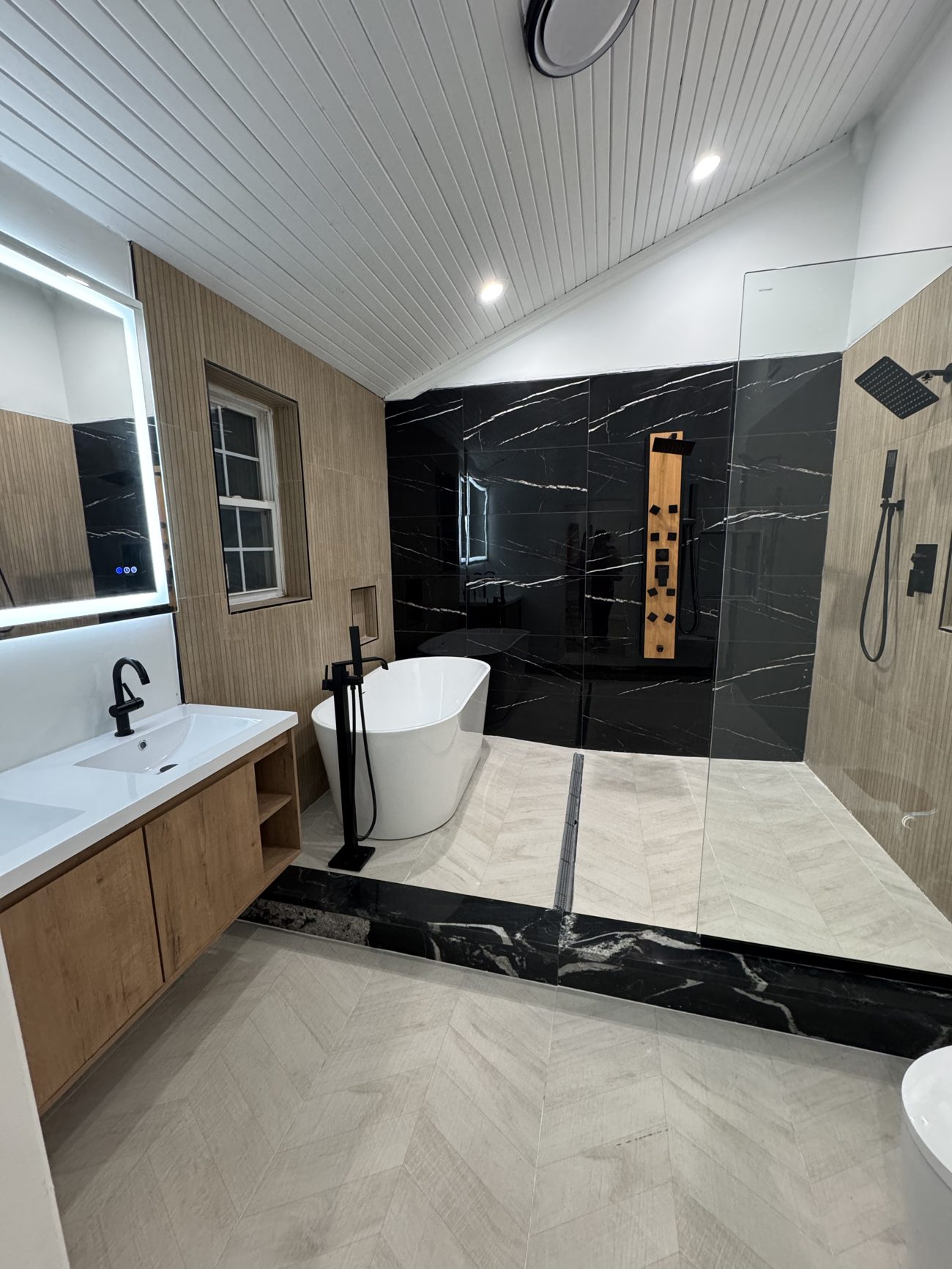 Modern primary bathroom remodel with black marble tile and freestanding tub