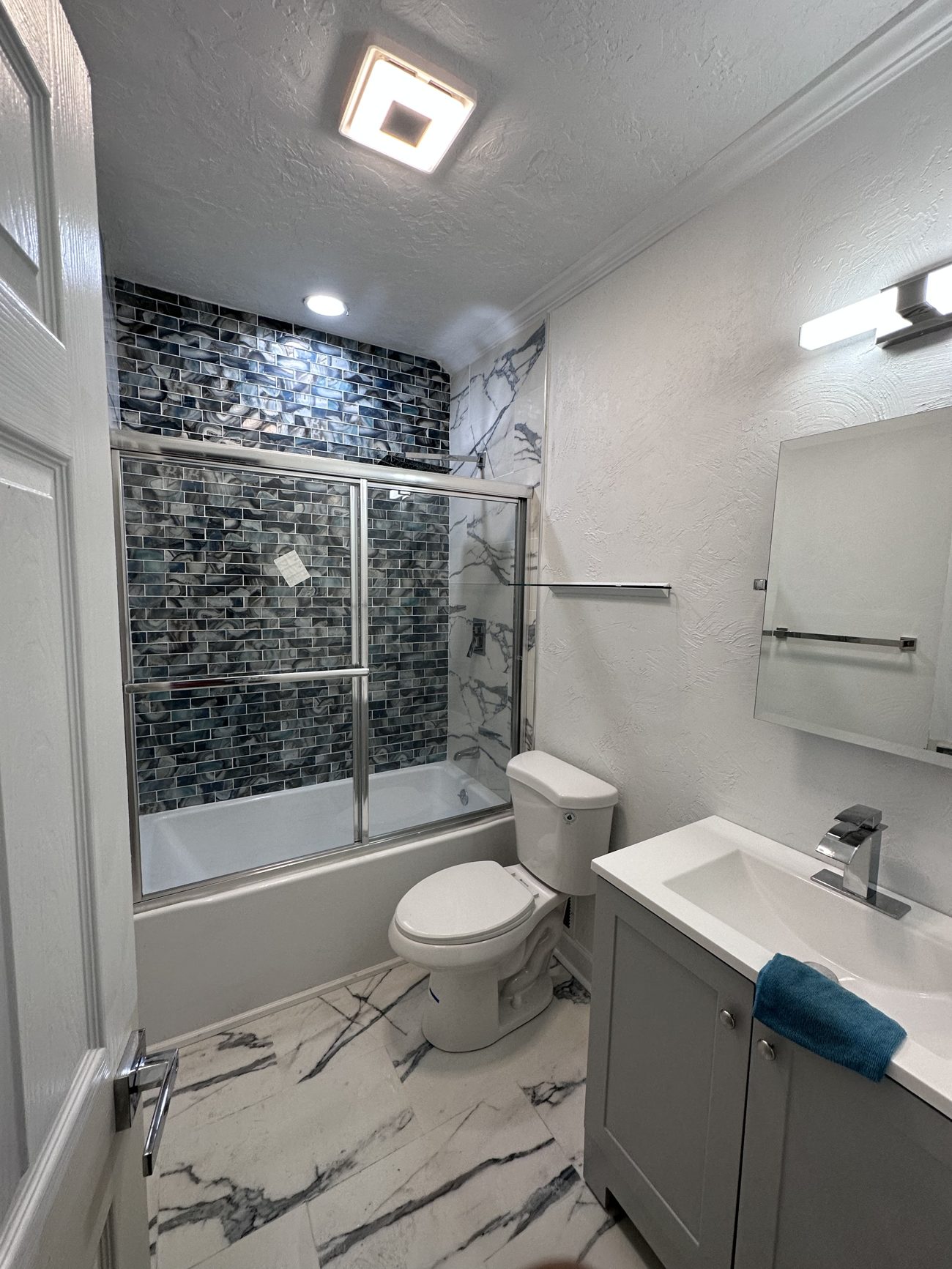 Walk-in tiled shower with glass mosaic and marble-look walls